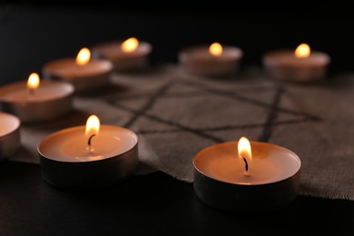 Photo of Fabric with star of David and burning candles on black background, closeup. Holocaust memory day