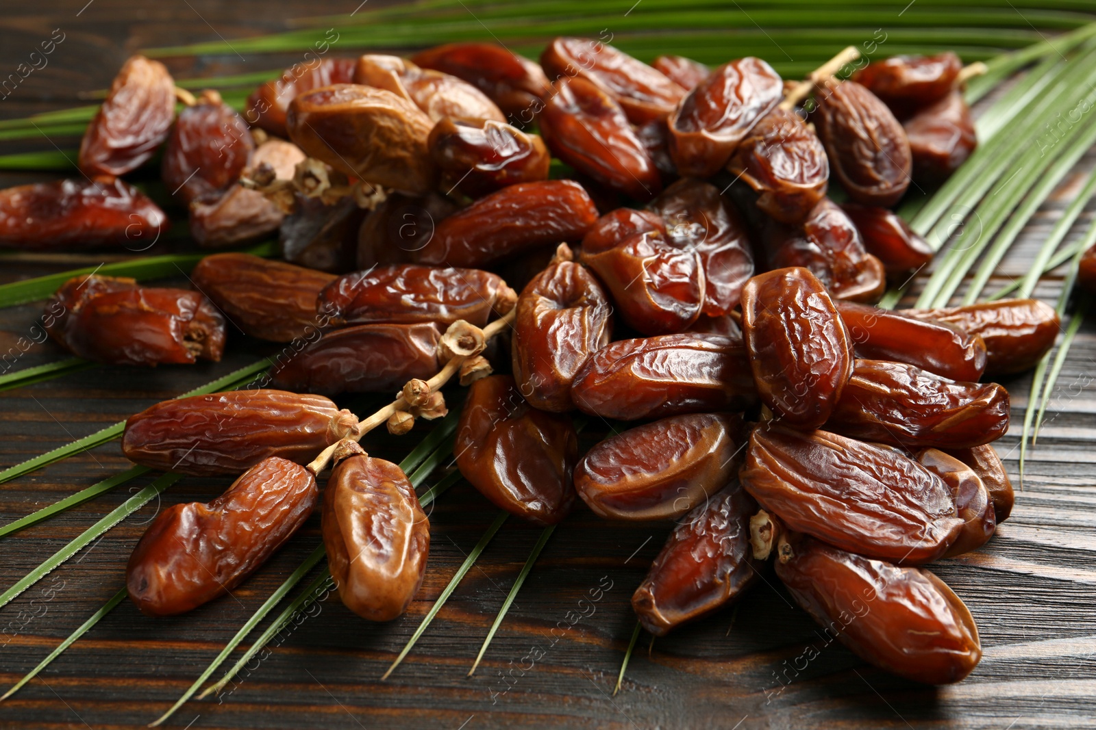 Photo of Tasty sweet dried dates and palm leaf on wooden table, closeup