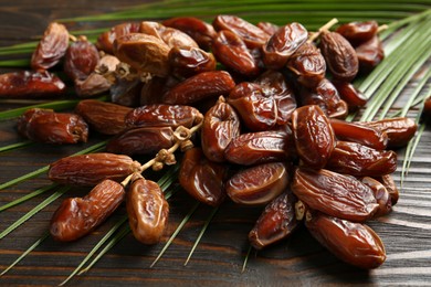 Photo of Tasty sweet dried dates and palm leaf on wooden table, closeup