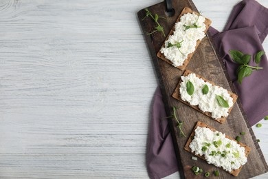 Photo of Crispy crackers with cottage cheese and different herbs on white wooden table, flat lay. Space for text