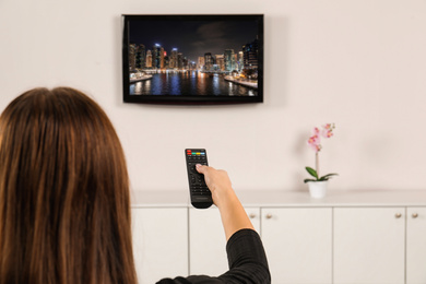 Woman switching channels on TV set with remote control at home