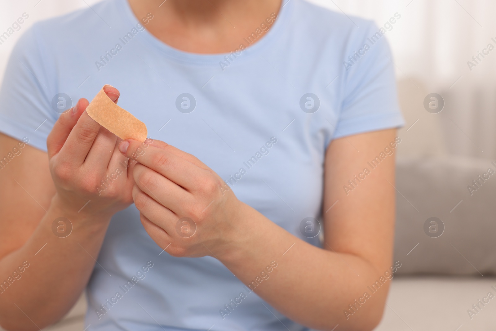 Photo of Woman putting sticking plaster onto finger indoors, closeup