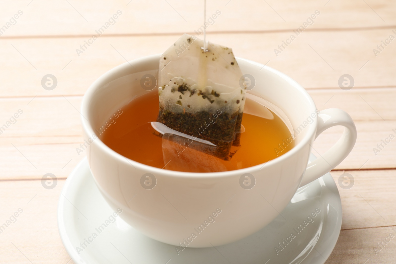 Photo of Putting tea bag in cup on light wooden table, closeup