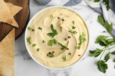 Photo of Delicious hummus with parsley and pita chips on white marble table, flat lay