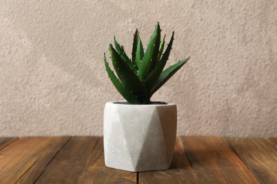 Beautiful artificial plant in flower pot on wooden table against grey background