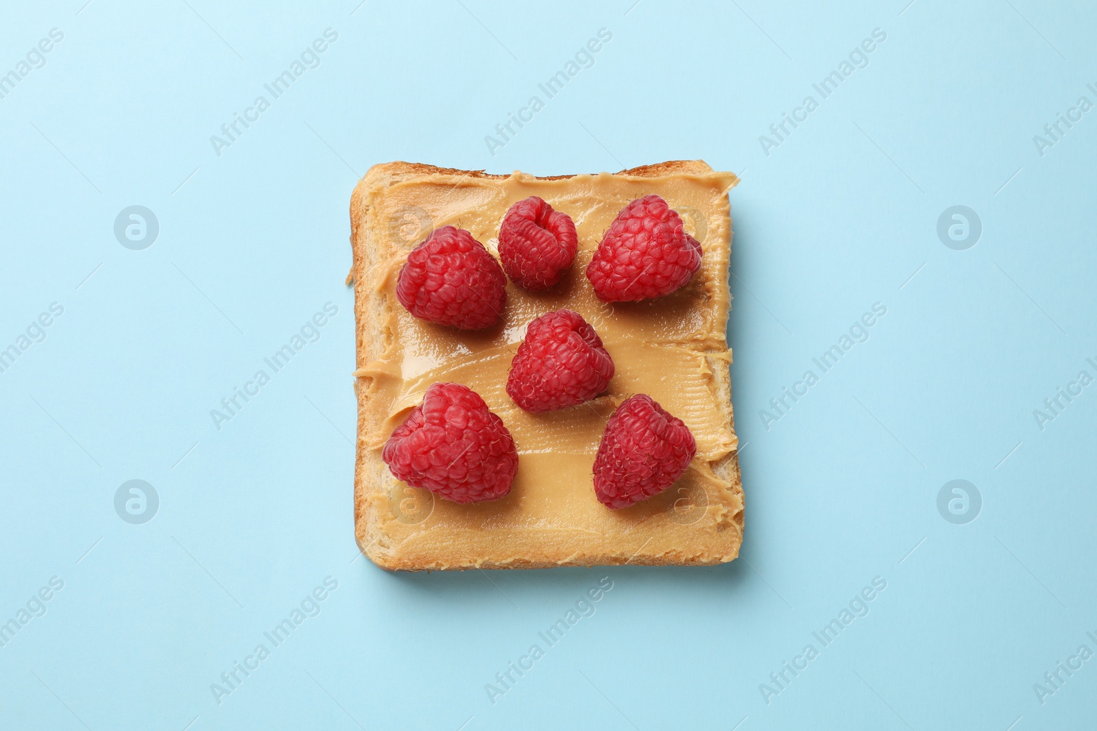 Photo of Tasty peanut butter sandwich with fresh raspberries on light blue background, top view