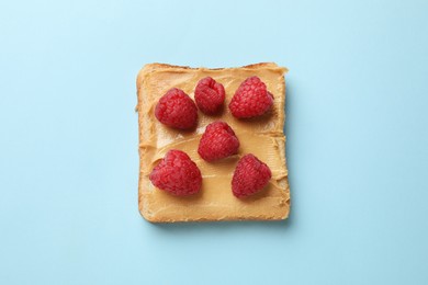 Photo of Tasty peanut butter sandwich with fresh raspberries on light blue background, top view