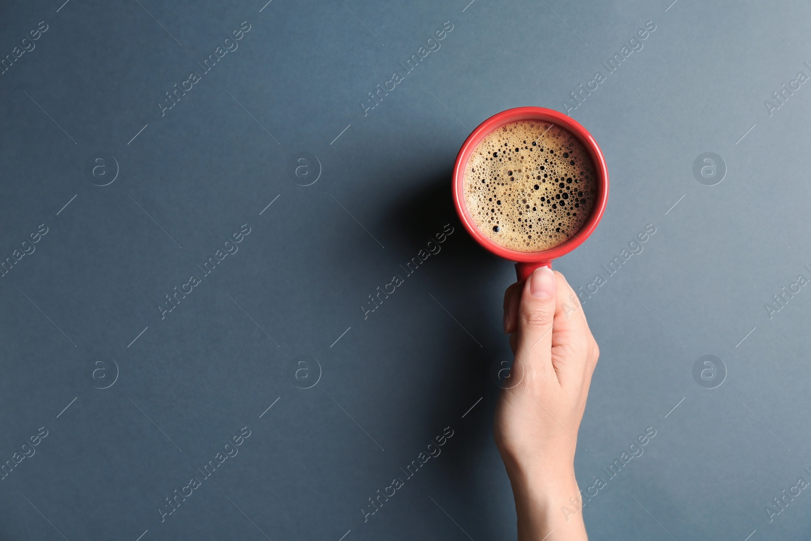 Photo of Young woman with cup of delicious hot coffee on grey background, top view