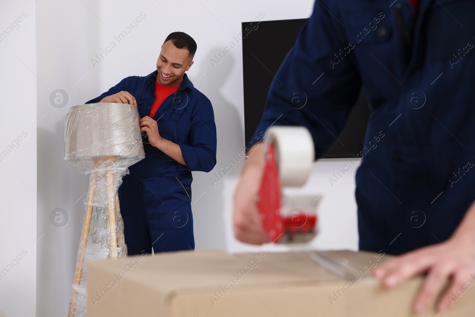 Photo of Male mover with stretch film wrapping floor lamp in house