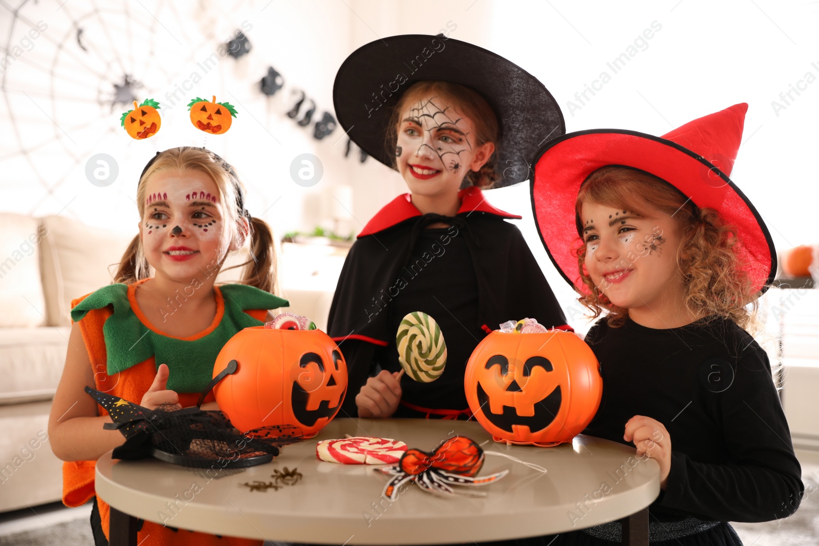 Photo of Cute little kids with pumpkin candy buckets wearing Halloween costumes at home