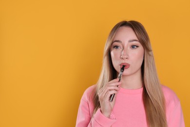 Young woman using electronic cigarette on orange background. Space for text