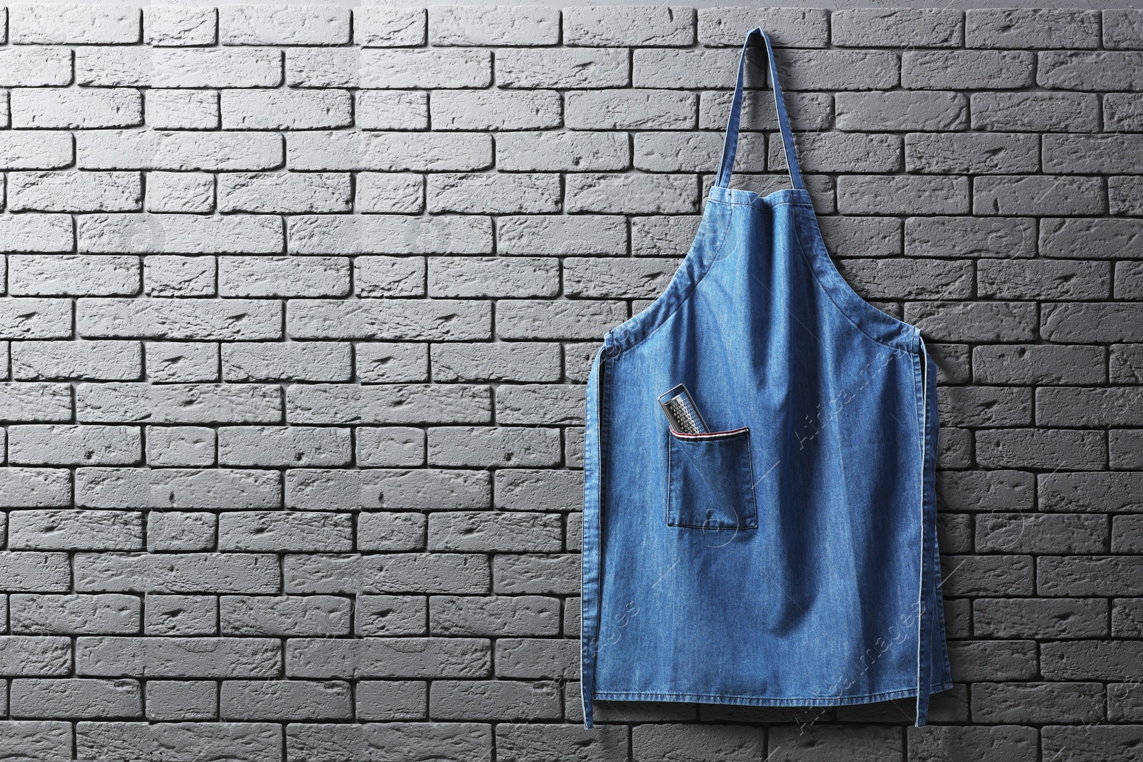 Photo of Clean denim apron with grater on grey brick wall