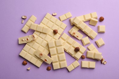 Photo of Delicious white chocolate with hazelnuts on violet background, flat lay