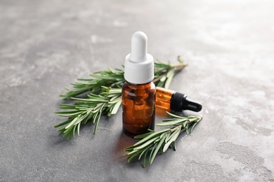 Photo of Bottle with rosemary essential oil on grey background