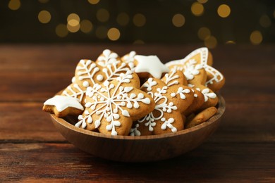 Tasty Christmas cookies with icing in bowl on wooden table against blurred lights