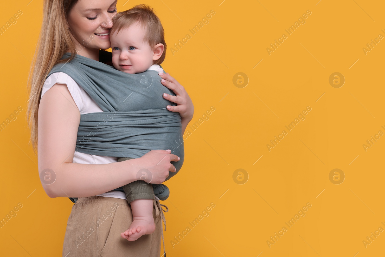 Photo of Mother holding her child in baby wrap on orange background, closeup. Space for text