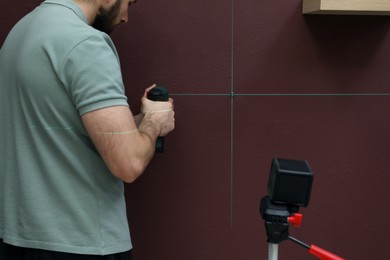 Man using cross line laser level for accurate measurement and drilling hole in brown wall, closeup
