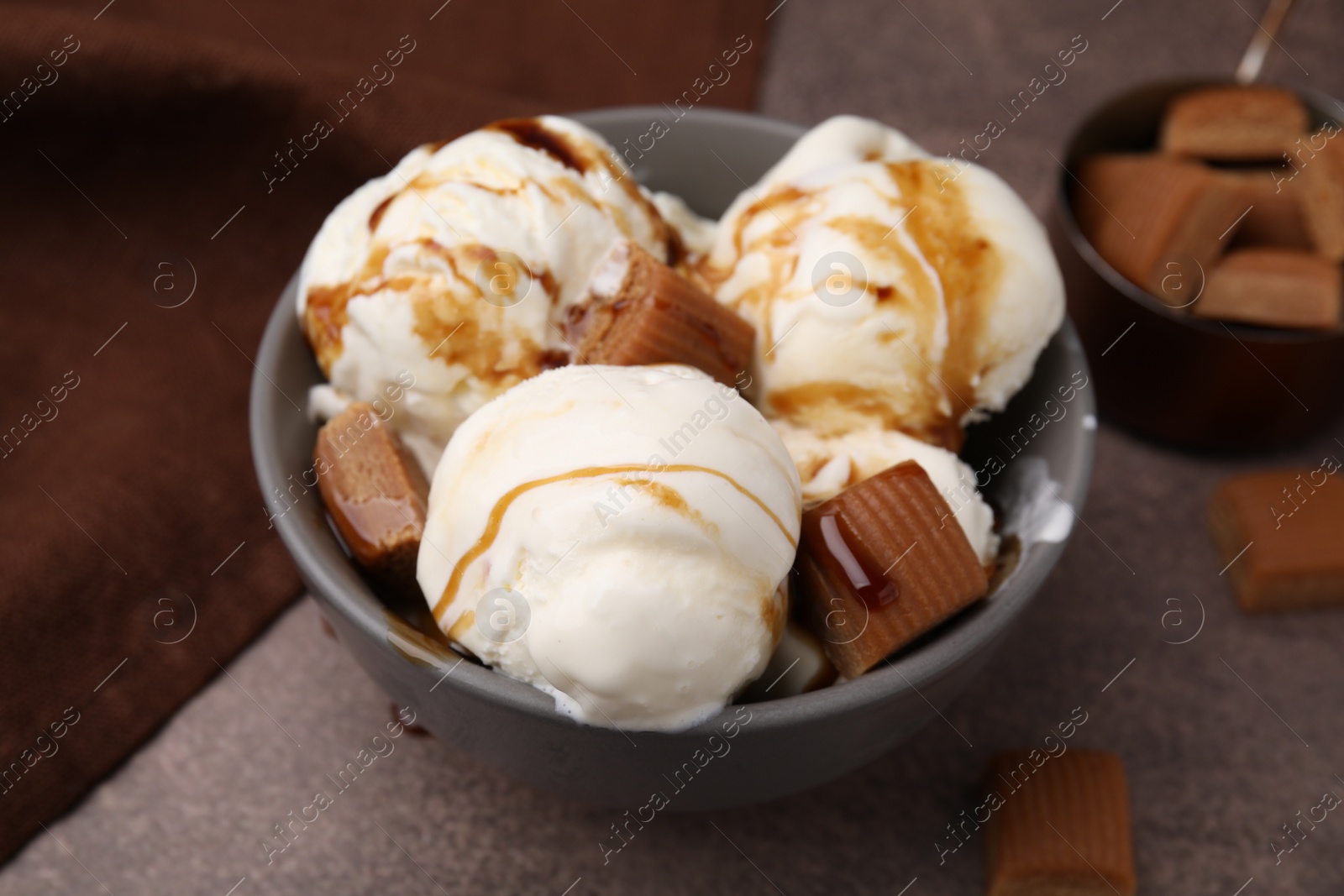 Photo of Scoops of ice cream with caramel sauce and candies on textured table, closeup