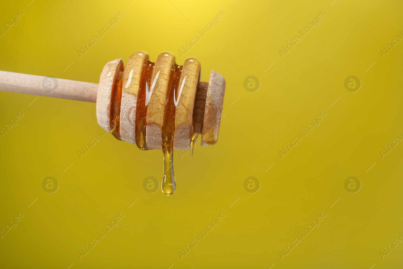 Photo of Delicious honey flowing down from dipper against golden background, closeup. Space for text