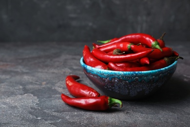 Photo of Bowl with red chili peppers on gray table. Space for text