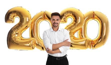 Happy young man near golden 2020 balloons on white background. New Year celebration