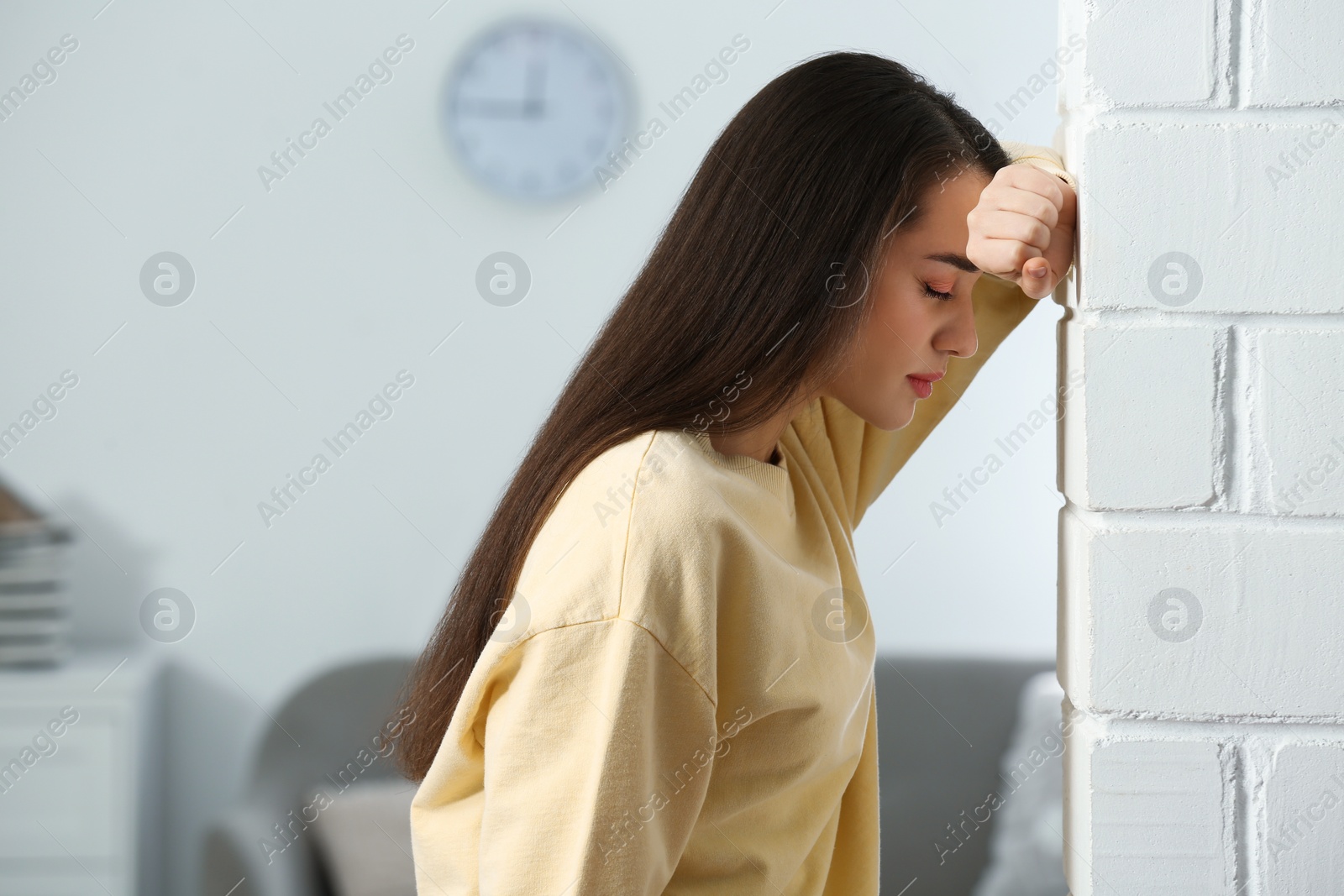 Photo of Stressed young woman near white brick wall at home