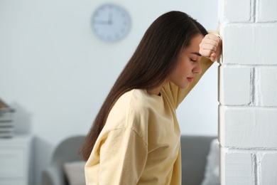 Photo of Stressed young woman near white brick wall at home