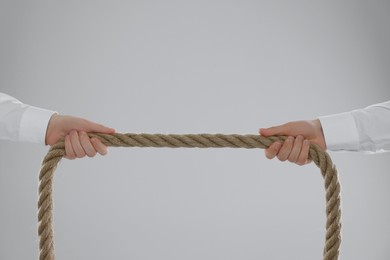 Dispute concept. Men pulling rope on light grey background, closeup