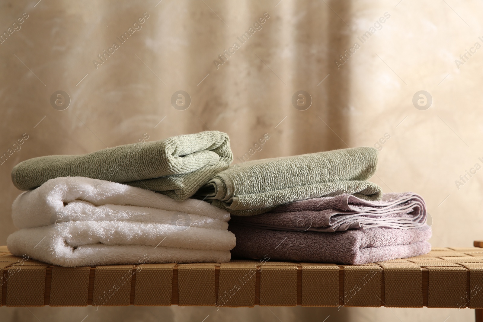 Photo of Stacks of soft towels on wicker bench indoors