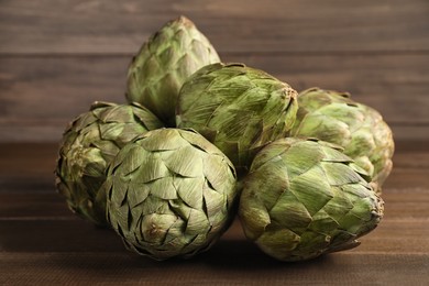 Many fresh raw artichokes on wooden table