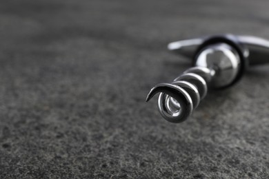 Photo of One metal corkscrew on grey textured table, closeup. Space for text