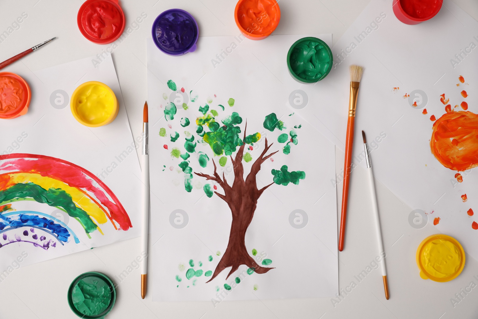 Photo of Cute children drawing, brushes and set of paints on white table, flat lay