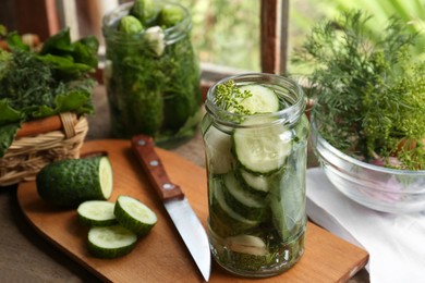 Photo of Glass jars, fresh cucumbers and herbs on wooden table indoors. Pickling recipe