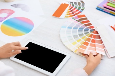 Photo of Woman with tablet and paint color palette samples at table, closeup