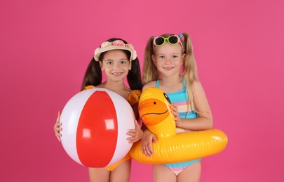 Photo of Cute little children in beachwear with bright inflatable toys on pink background