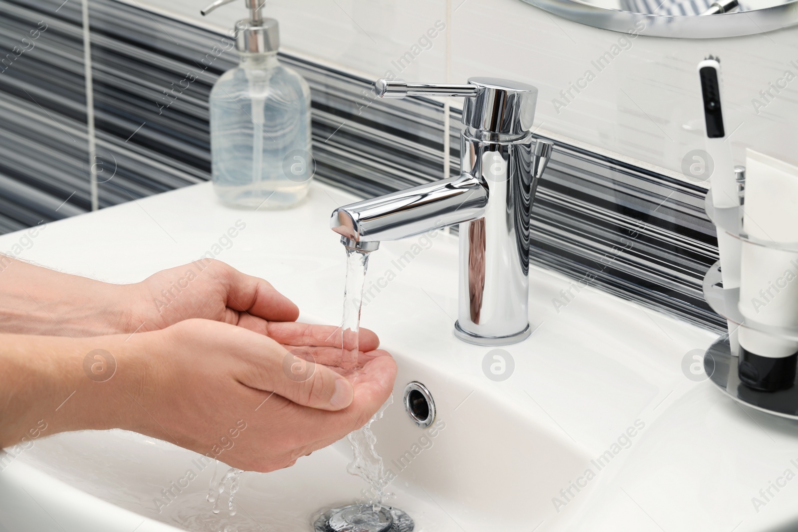 Photo of Man using water tap to wash hands in bathroom, closeup