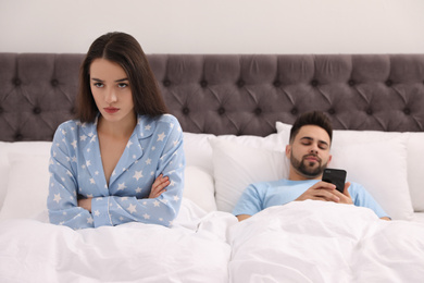 Young man preferring smartphone over his girlfriend in bed at home
