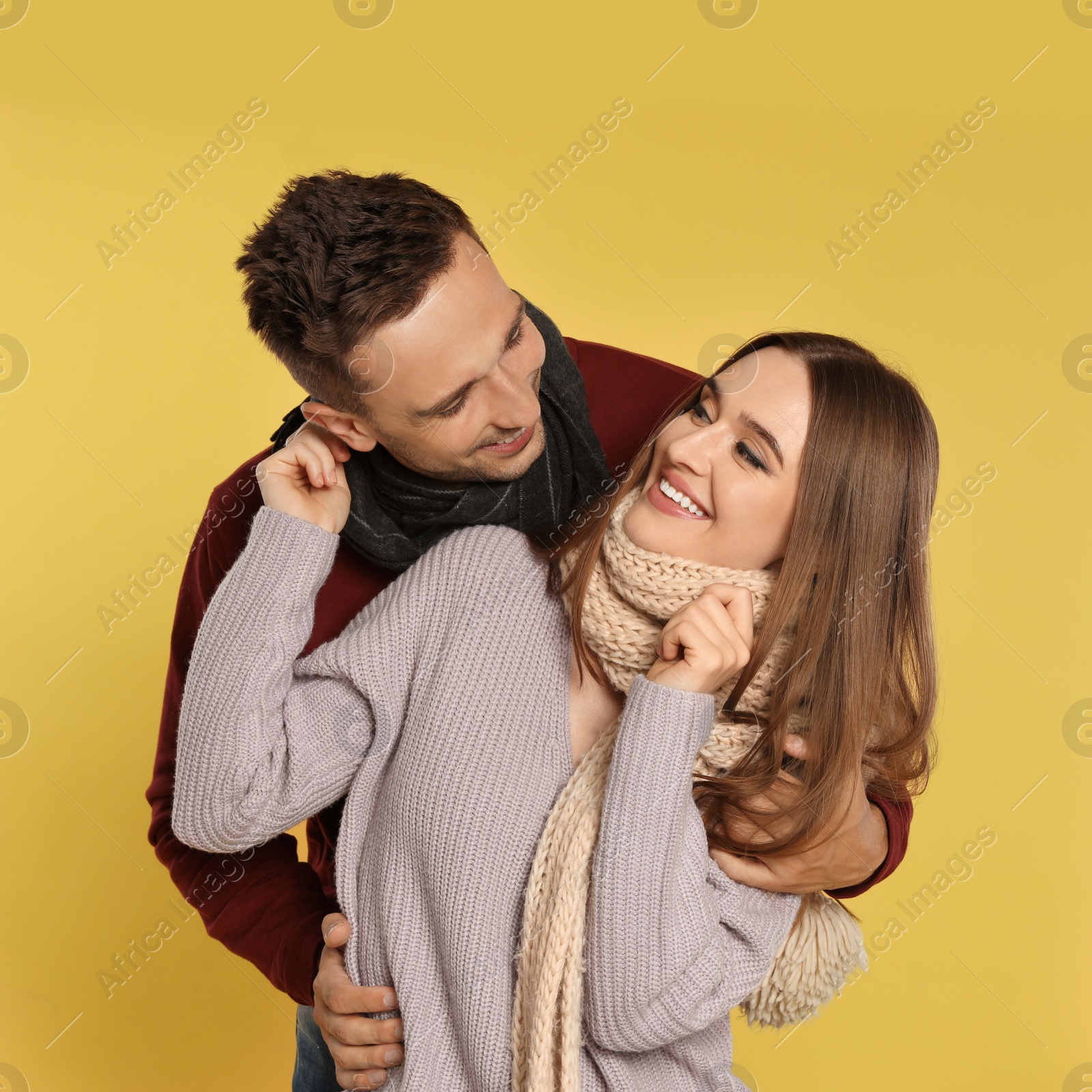 Photo of Happy young couple in warm clothes on yellow background. Winter season