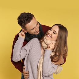 Photo of Happy young couple in warm clothes on yellow background. Winter season
