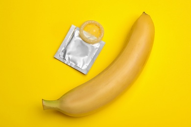 Photo of Condom and banana on yellow background, flat lay. Safe sex