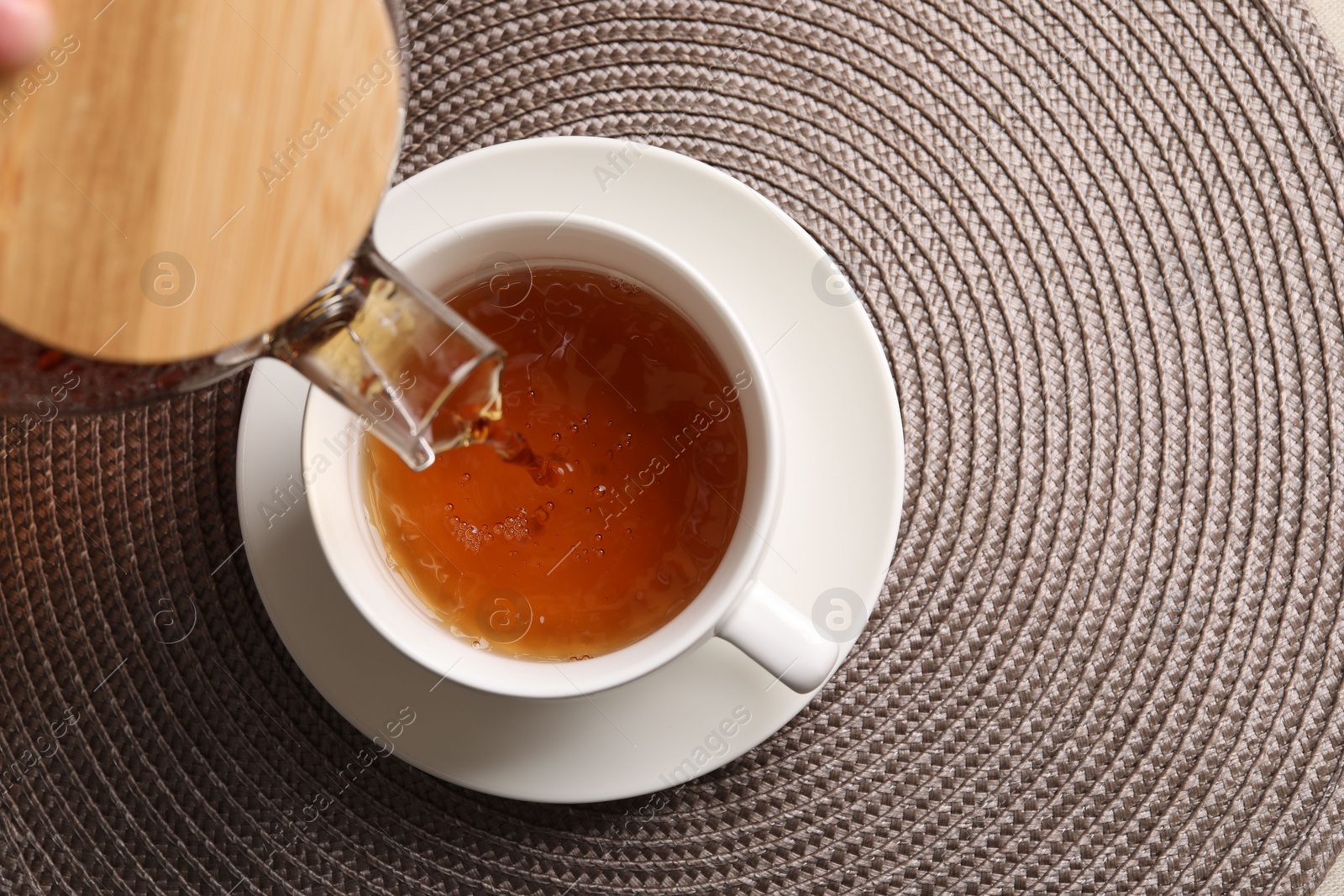 Photo of Pouring aromatic tea into cup at table, top view. Space for text