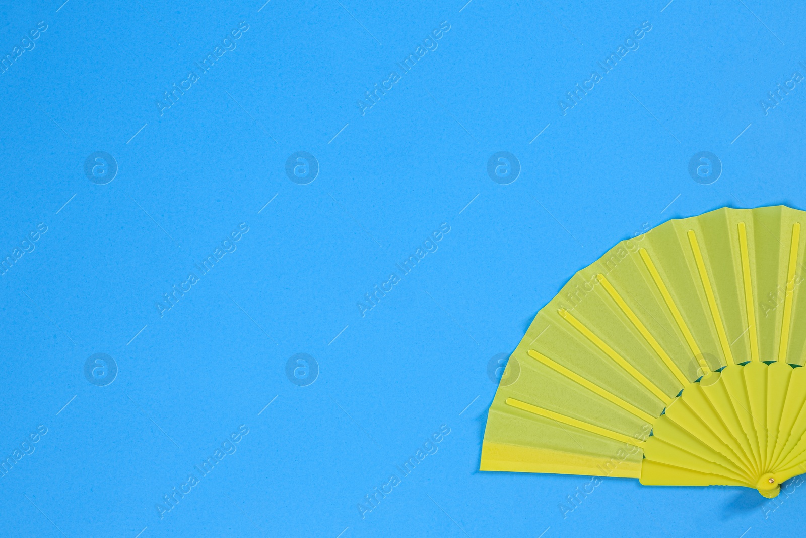 Photo of Yellow hand fan on light blue background, top view. Space for text