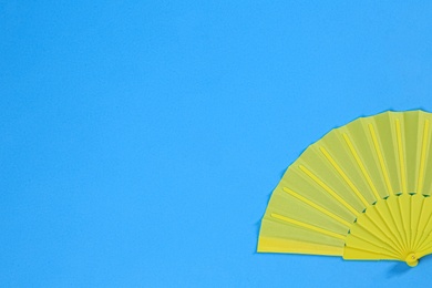 Yellow hand fan on light blue background, top view. Space for text