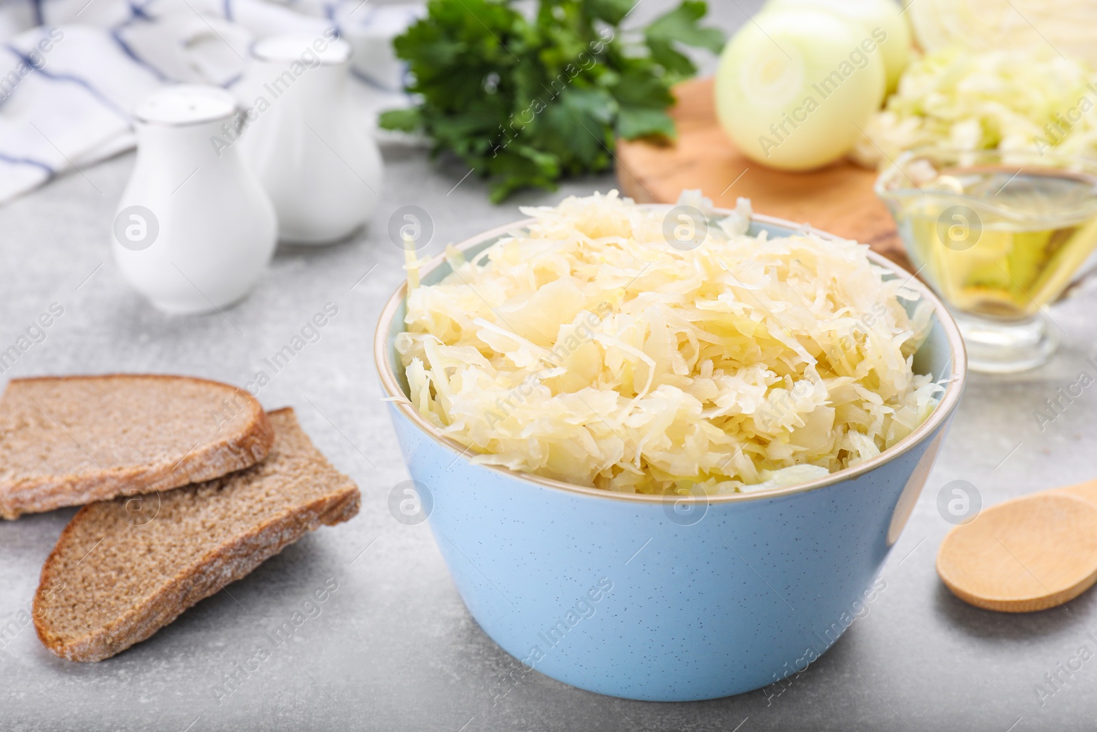 Photo of Bowl of tasty sauerkraut and ingredients on grey table