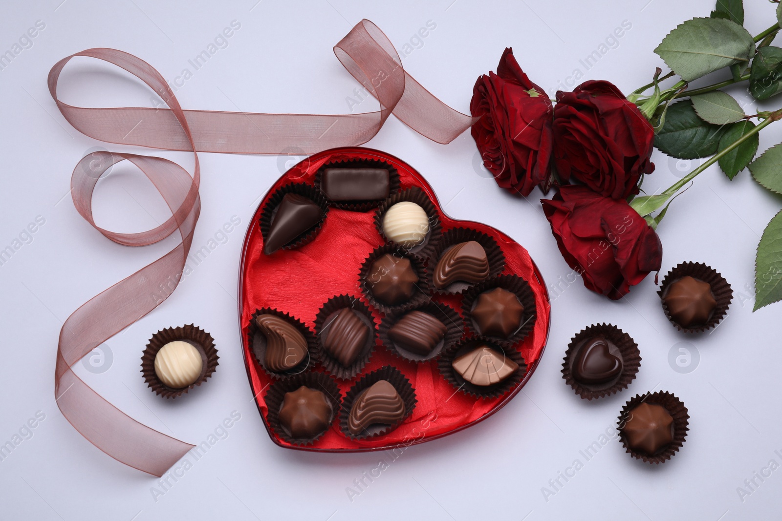 Photo of Heart shaped box with delicious chocolate candies, roses and ribbon on white background, flat lay