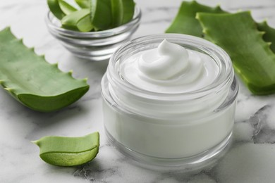 Jar with cream and cut aloe leaves on white marble table, closeup