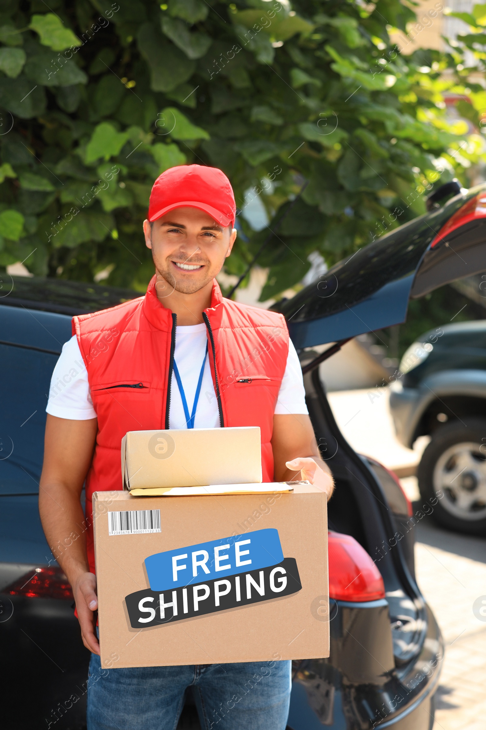 Image of Young courier holding parcels near car outdoors. Free shipping
