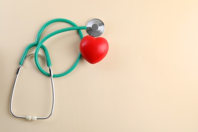 Stethoscope and red heart on beige background, top view. Space for text