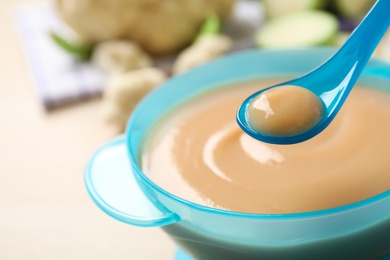 Photo of Spoon of healthy baby food over bowl on table, closeup