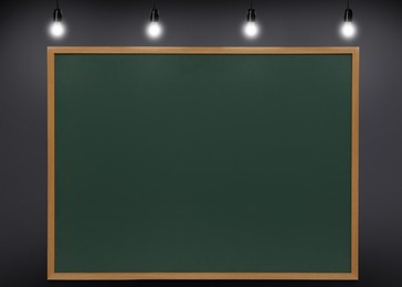 Image of Glowing light bulbs and green chalkboard hanging on grey wall